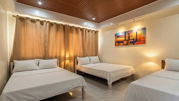 Habitación de hotel con tres camas individuales, techo de madera, un cuadro en la pared y una cortina.