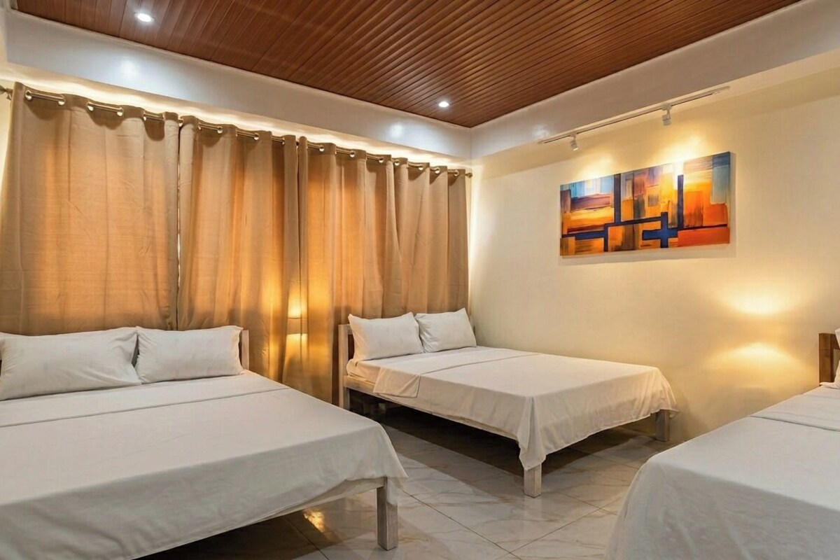 Habitación de hotel con tres camas individuales, techo de madera, un cuadro en la pared y una cortina.