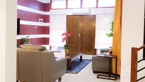 Un salón moderno con un sofá, una mesa de centro y una mesita con adornos. Se observa una puerta de madera y una ventana con cortinas.
