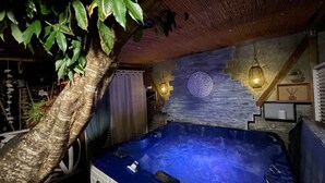Ein Bereich mit Whirlpool, einem Baum, einer Steinmauer und einer Holzbalkendecke.