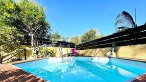 Ein Schwimmbecken mit Holzterrasse, einer Metallleiter und einer Palme im Hintergrund.