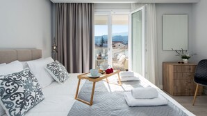 Una habitación de hotel moderna con una cama grande, una mesita de madera con una bandeja, un balcón con vistas al campo y un armario de madera.