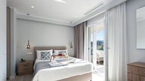 Un dormitorio moderno con una cama grande, mesitas de noche, un aparador de madera y un balcón con cortinas.