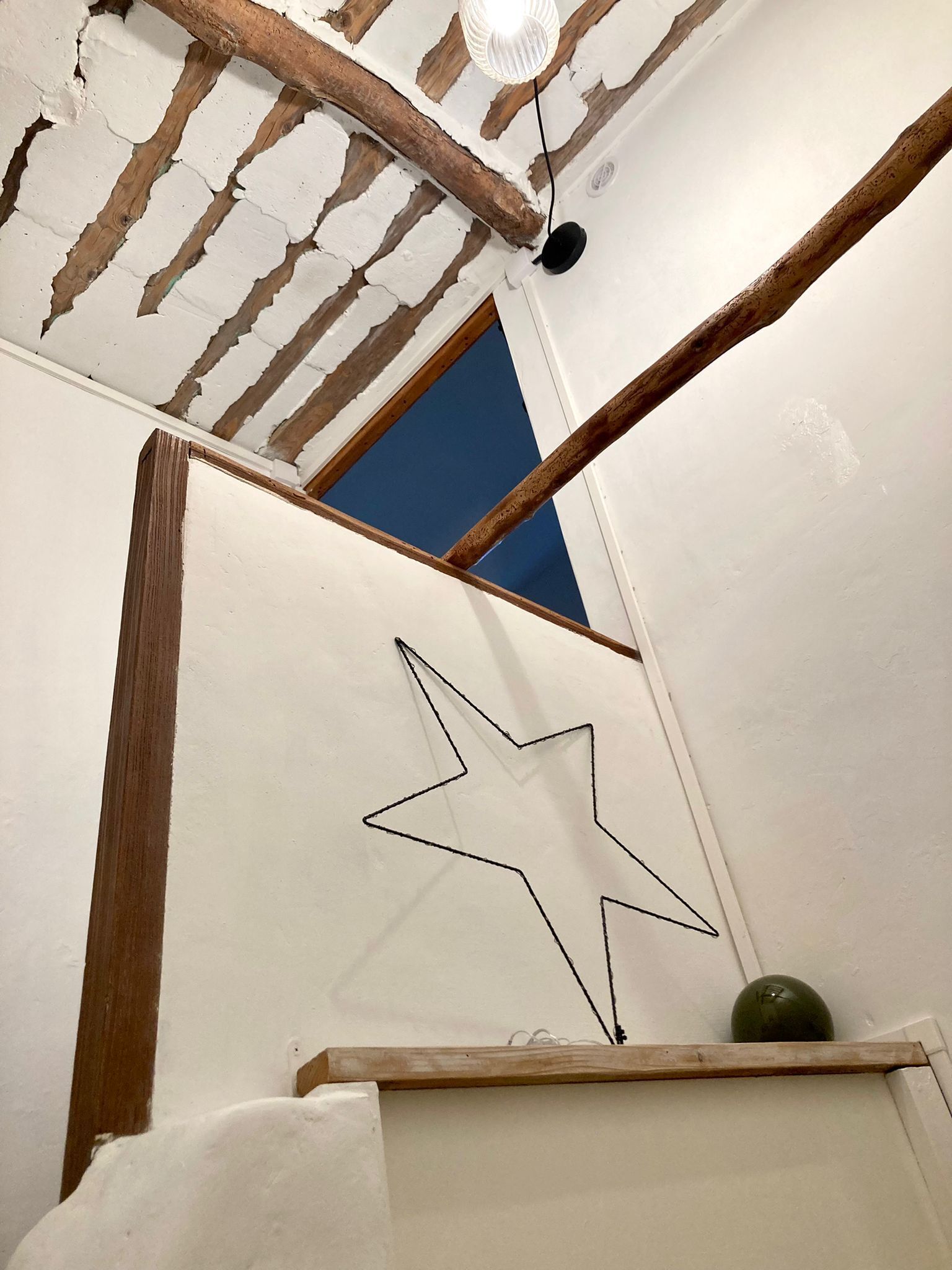 A room with exposed wooden beams, a white wall with a star outline, and a blue door.