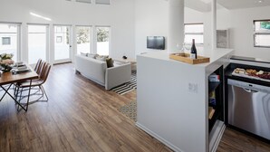 Eine moderne Küche mit Einbauofen, ein Essbereich mit Holztisch und Stühlen sowie eine Sitzecke mit Sofa und Couchtisch.