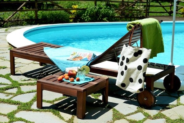 A poolside area with lounge chairs, a small table with fruits and a drink, and a polka-dotted bag. - Delightful family Farmhouse with pool, in the woods, 20 km from Florence (Toscana)