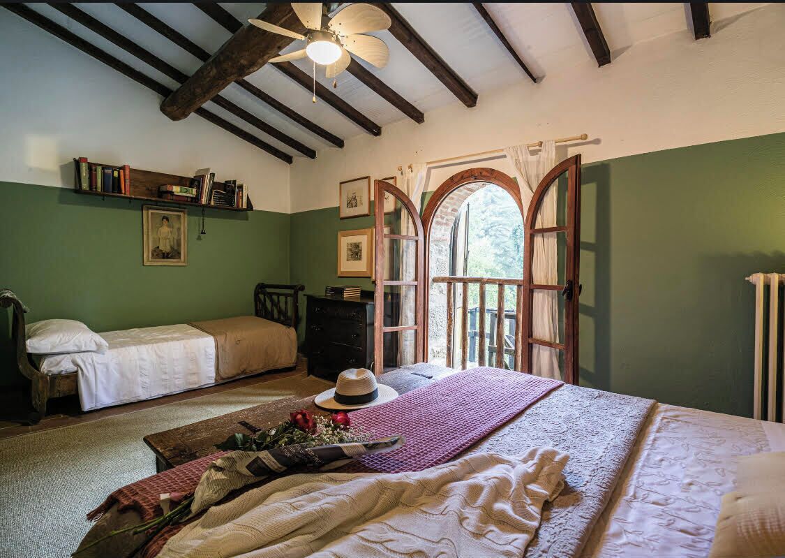 A cozy room with a bed, a wooden dresser, a bookshelf, and a window with an arched design.