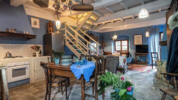 A rustic kitchen with a stone floor, wooden furniture, and a staircase leading to another level.