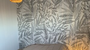 Ein Schlafzimmer mit einem Bett, einem Nachttisch, einer Wandlampe und Tapete mit Blätermotiv.