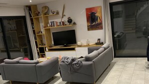 Ein modernes Wohnzimmer mit zwei grauen Sofas, einem Fernseher und einem Bücherregal.