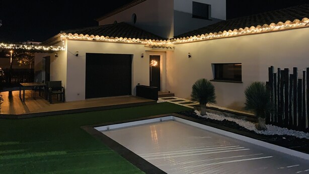 Ein modernes Haus mit überdachter Terrasse, Swimmingpool und gut beleuchteter Fassade.