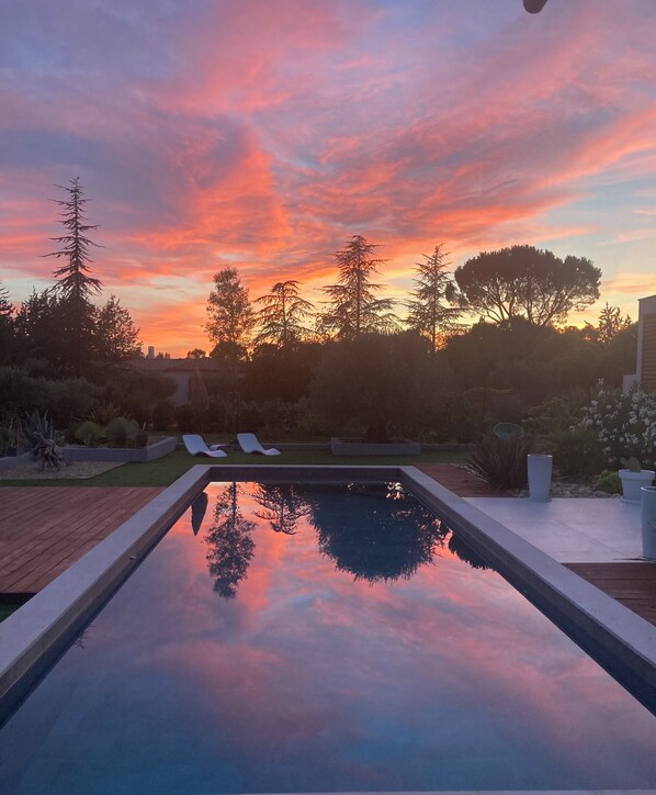 A swimming pool reflecting a sunset sky, surrounded by trees and a patio area.