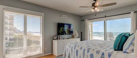 Un dormitorio con una cama grande, ventilador de techo, televisor y vista a la playa.
