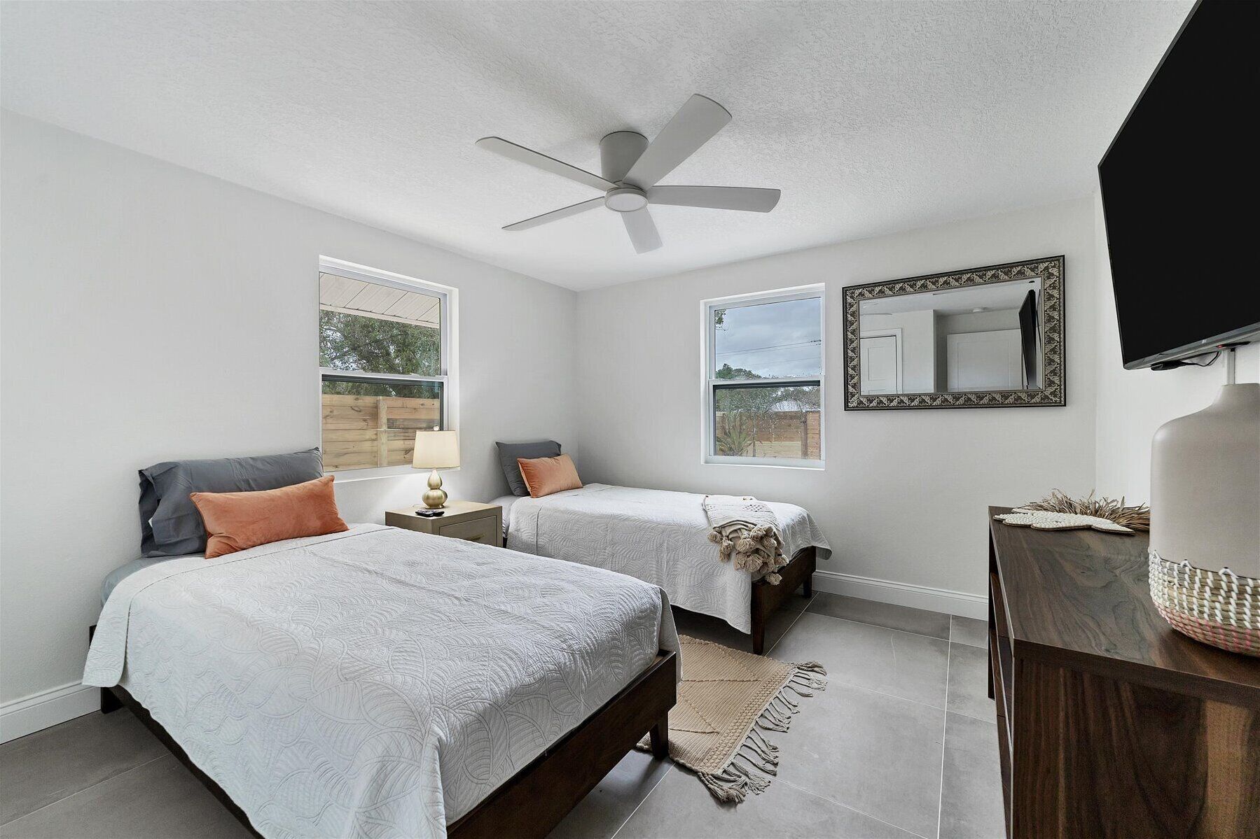 A bedroom with two beds, a ceiling fan, a large mirror, and a TV.