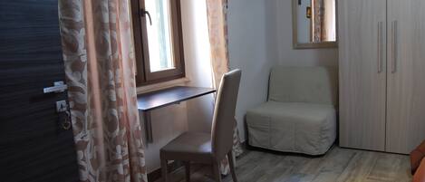 A room with a wooden desk, a chair, a wardrobe, and a window with curtains.