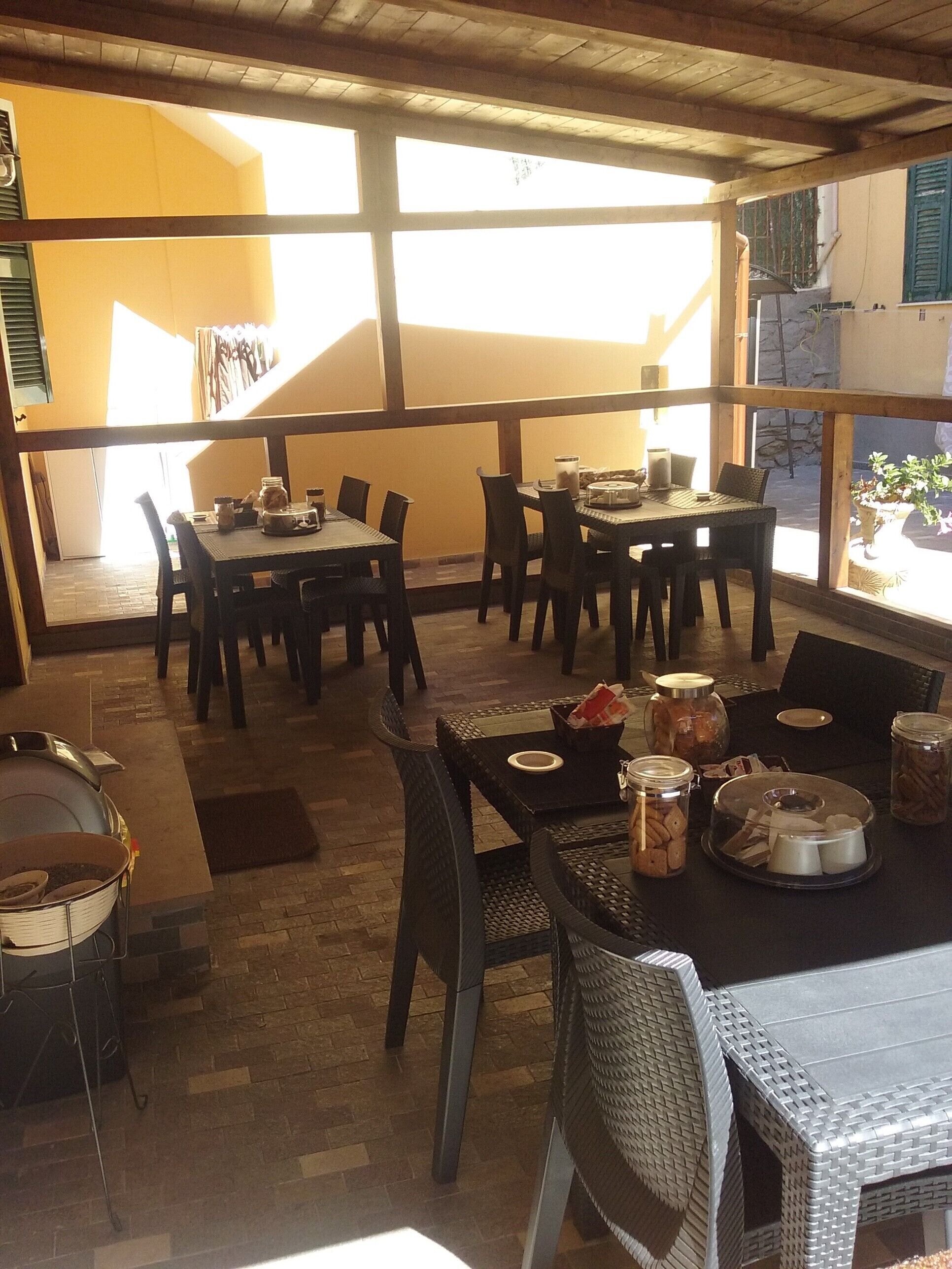 Een eetruimte met tafels en stoelen, een buffetopstelling met potten en borden, en uitzicht op buiten door grote ramen.