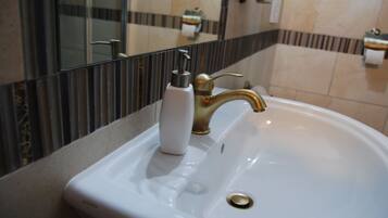 A white bathroom sink with a gold faucet and a soap dispenser.