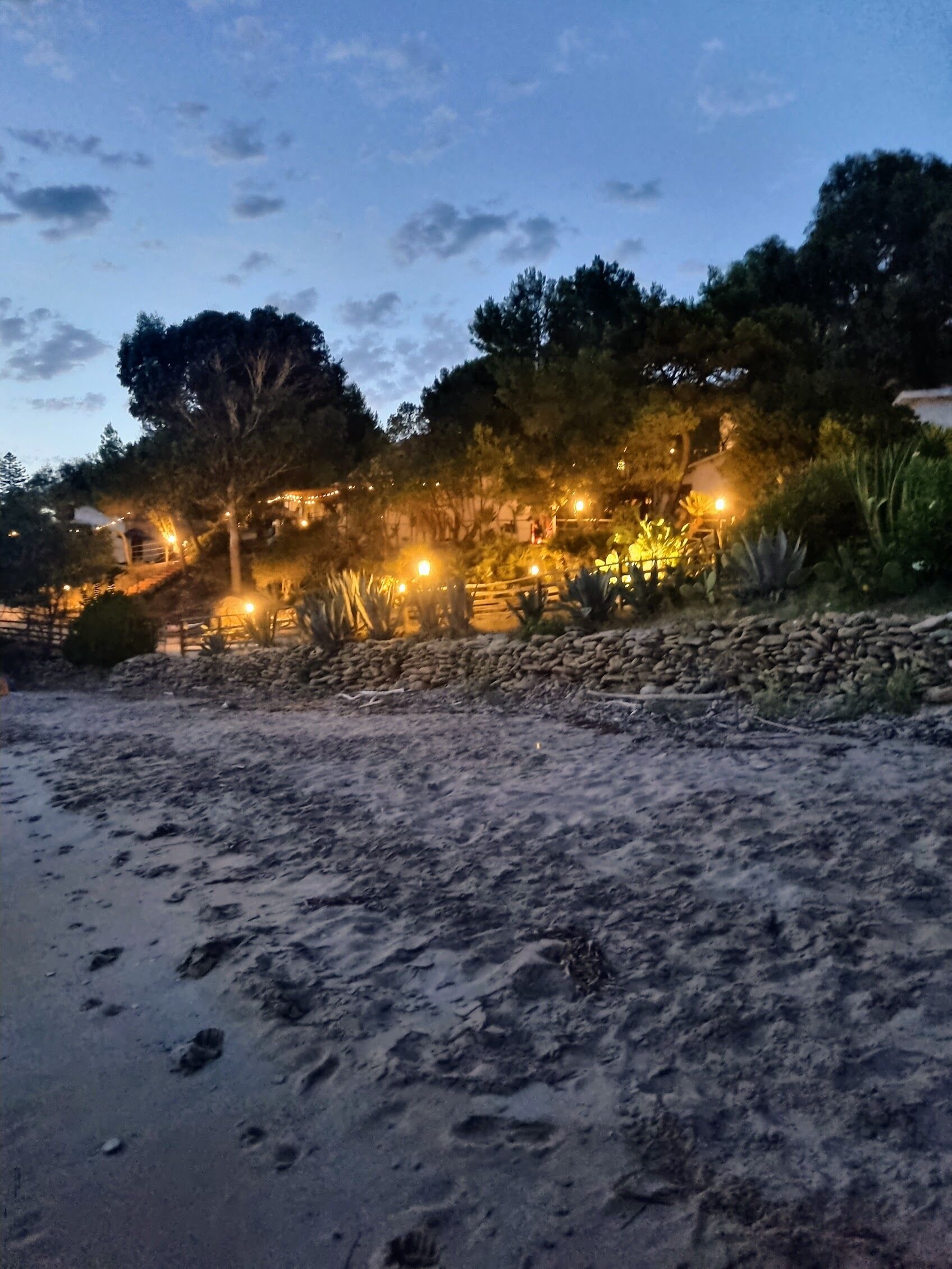 Uma praia com um muro de pedra e árvores. Há luzes ao longo do muro.