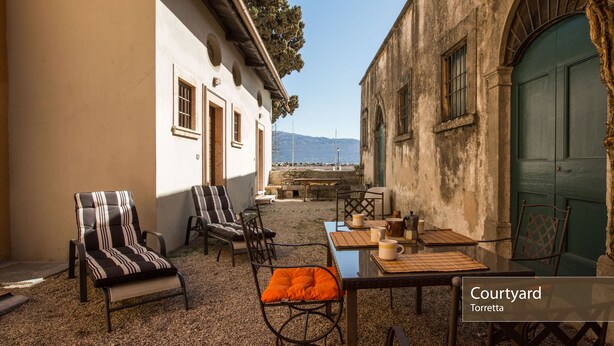 Un patio con una mesa y sillas, vista al mar y un edificio con una puerta verde.