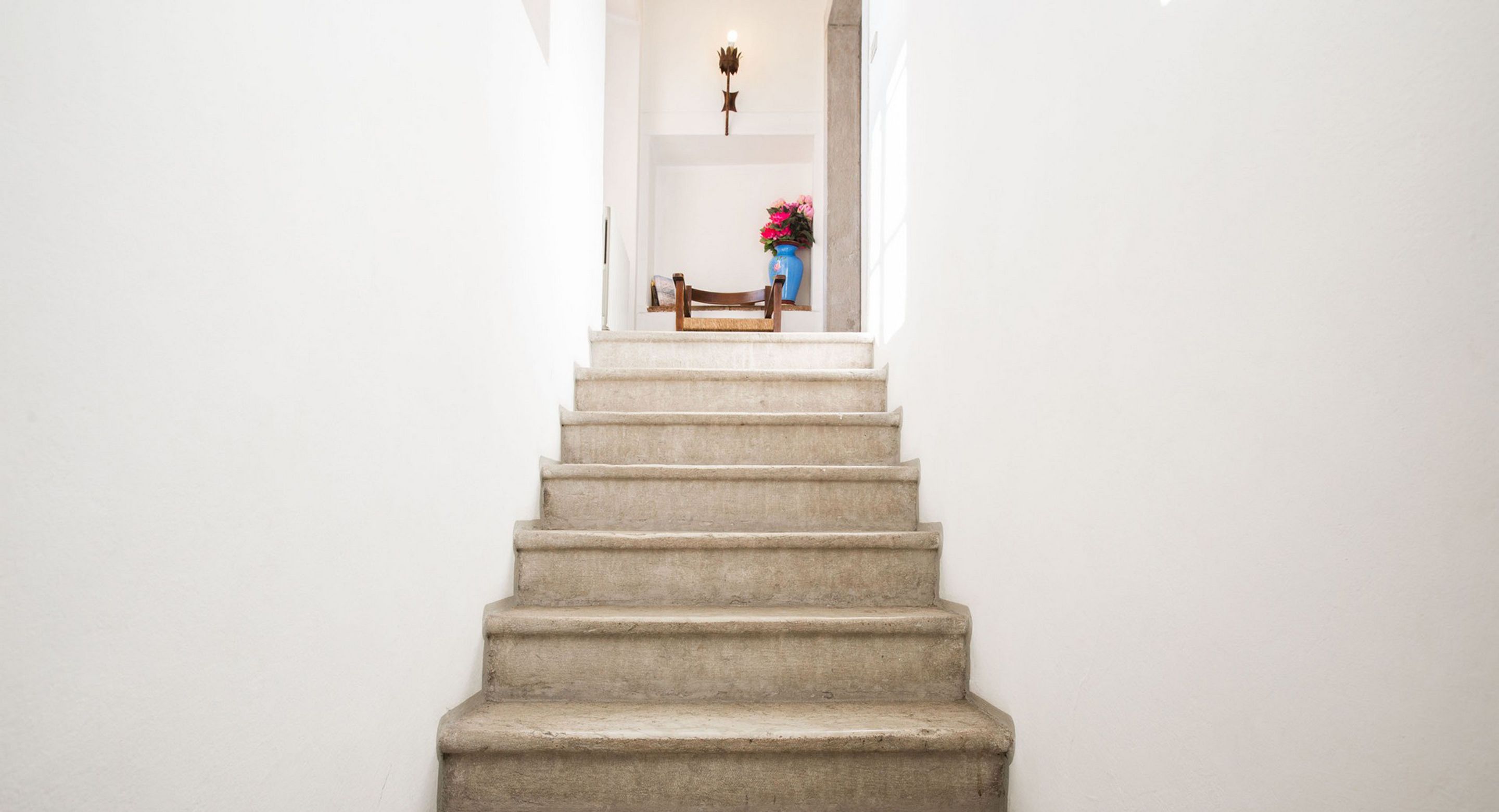 Un escalier menant à un palier où se trouvent un banc et un vase de fleurs.