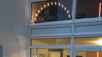 Ein verschneiter Außenbereich mit einem dekorativen Schneemann und Lichter, vor einem Gebäude mit großen Glasfenstertüren.