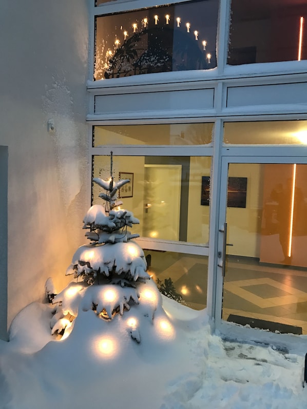 Ein verschneiter Außenbereich mit einem dekorativen Schneemann und Lichter, vor einem Gebäude mit großen Glasfenstertüren.