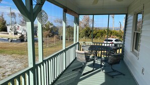 A covered porch with a table and chairs, a ceiling fan, and a view of the surrounding area including a boat and a car.