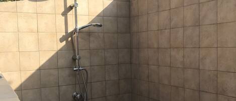 Un petit espace douche fermé, avec des murs carrelés et une pomme de douche en métal.