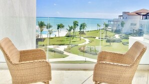 A balcony with two wicker chairs, a clear view of the ocean, and a landscaped garden. - G-34B Cap Cana Punta Palmera Beach Studio Ocean View NEW! (Punta Cana)