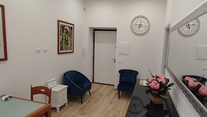 A modern room with a wooden table, two blue chairs, a white dresser, a mirror, and a potted plant. - Maria in Vaticano (Rome)