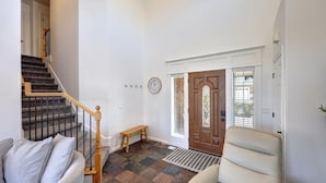 Una entrada limpia y bien iluminada con una escalera de madera, un banco y una puerta con un panel de vidrio decorativo.