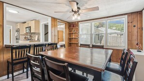 A dining area with a large wooden table and chairs, a ceiling fan, and a view of the kitchen and outside through large windows. - Affordable & Spacious home near Minneapolis (Minneapolis)