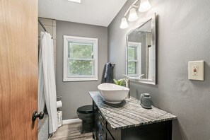 Une salle de bain avec un lavabo blanc, un porte-serviettes, un miroir et une fenêtre avec des stores.