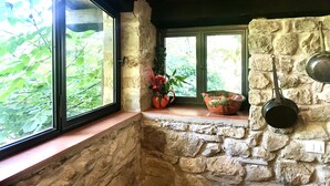 A stone-walled kitchen with large windows, a hanging light fixture, and a window seat with potted plants. - Adorable retreat in the woods with pool, near Florence! (Toscana)