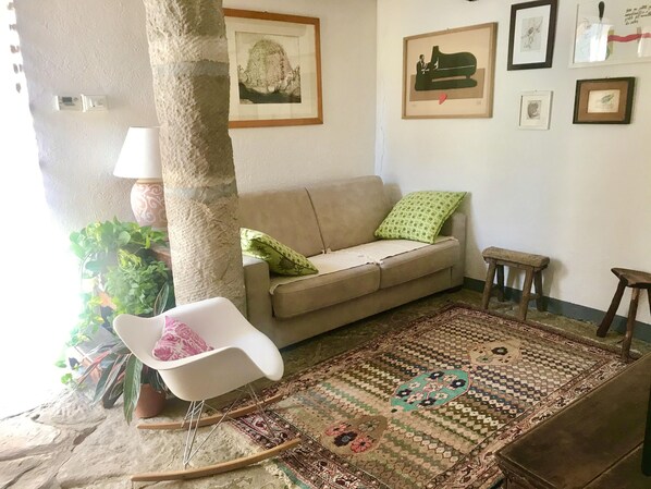 A living room with a beige sofa, a rocking chair, a patterned rug, and a green cushion.