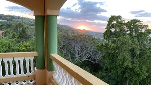Varanda com vista para um pôr do sol sobre uma paisagem montanhosa.