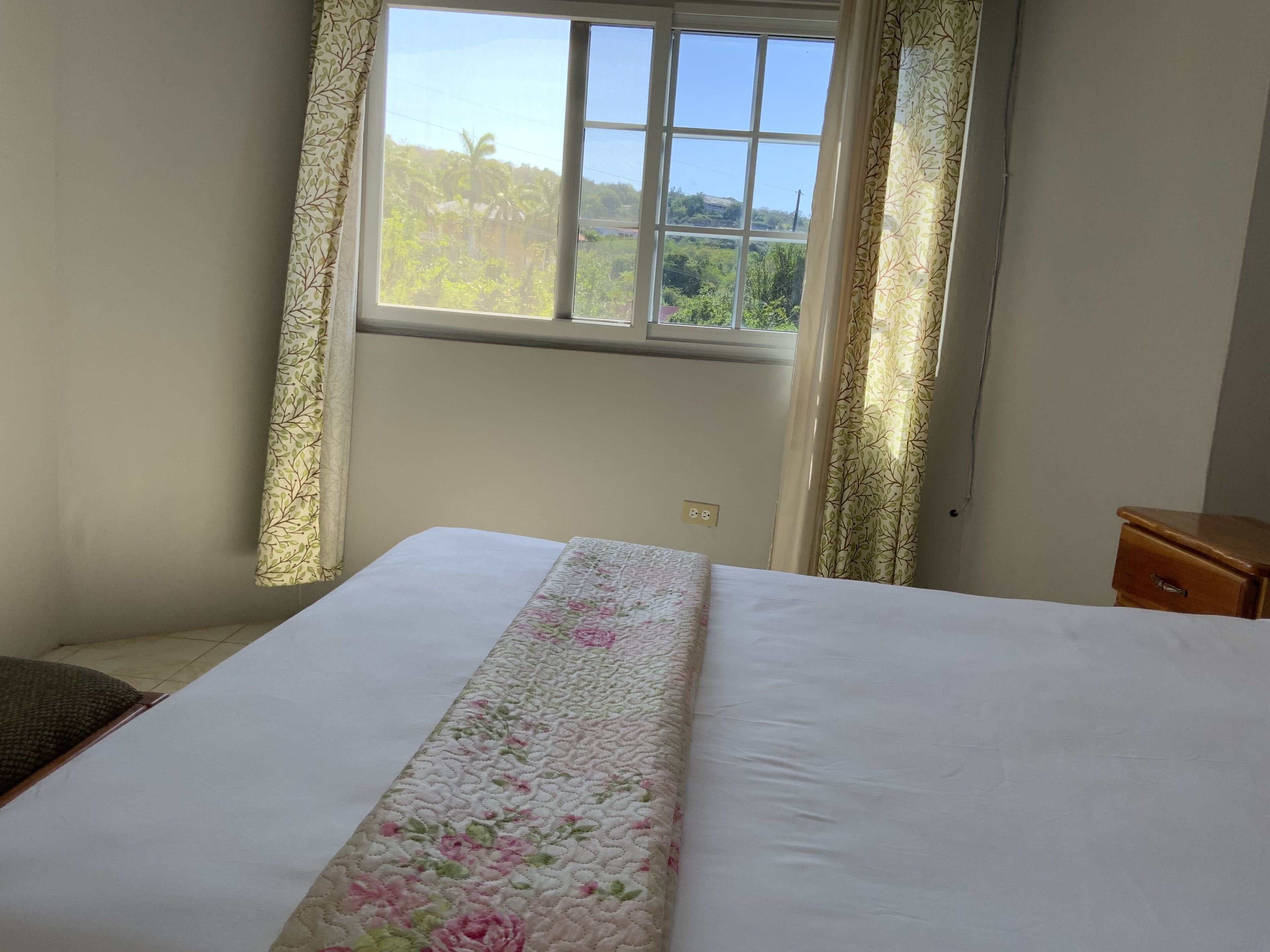 A bedroom with a bed, a window with curtains, and a nightstand.