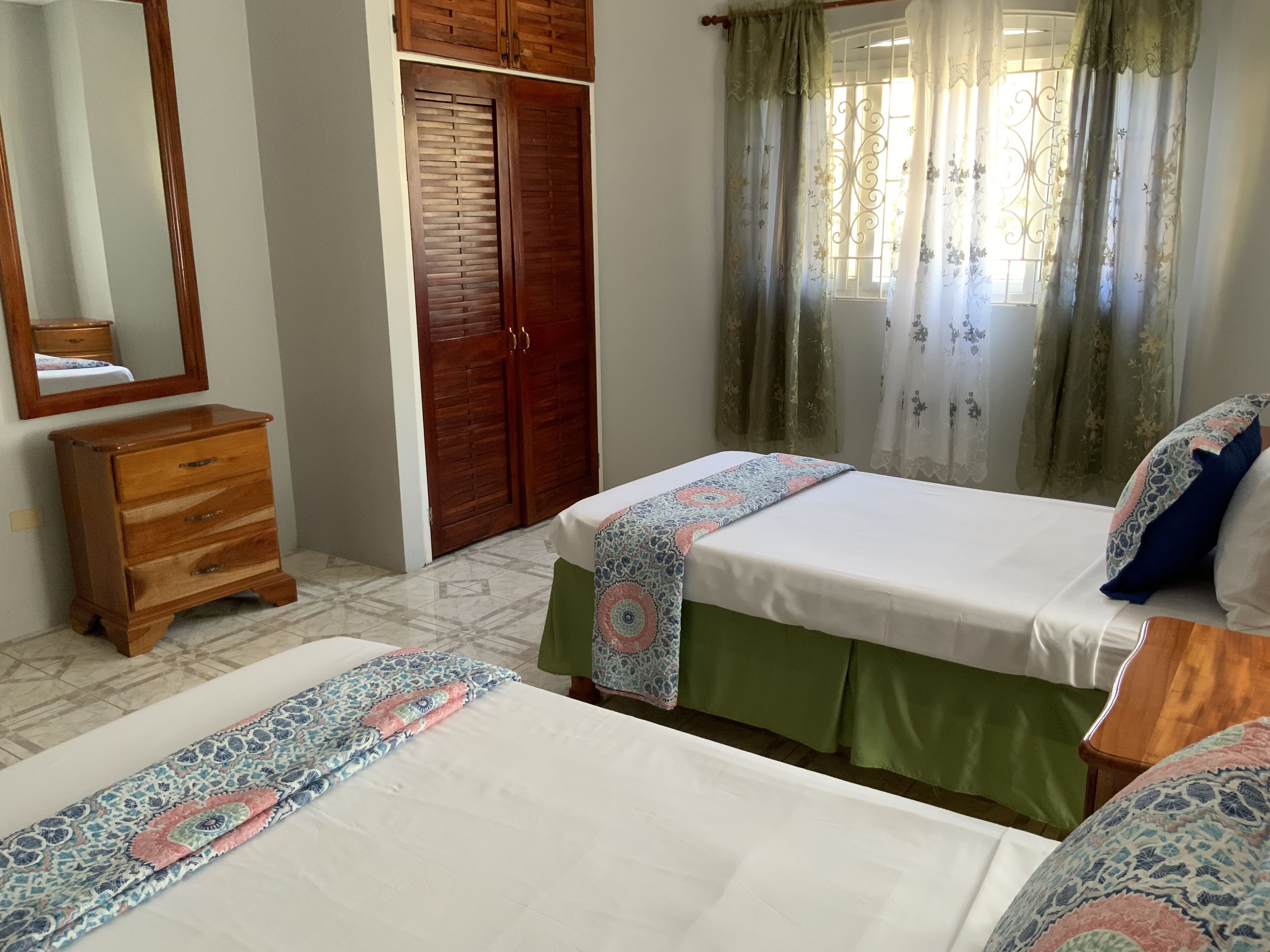 Une chambre avec deux lits, une commode en bois, une armoire et une fenêtre avec des rideaux.