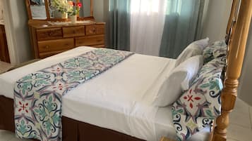A neatly made bed with a patterned bedspread, a wooden dresser with a mirror, and a vase with flowers.