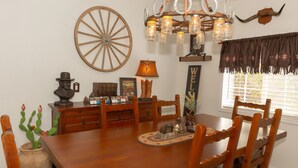 A wooden dining table with chairs, a chandelier, a large wooden wheel, and a 'WELCOME' sign.