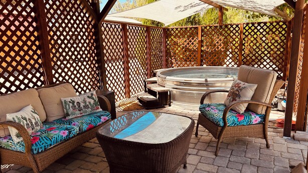 An outdoor patio area with wicker furniture, a hot tub, and a wooden pergola.