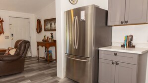 A modern kitchen with a stainless steel refrigerator, wooden flooring, and a white countertop.