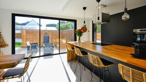 A modern kitchen with a wooden island, bar stools, and a large window overlooking a deck. - A 2 pas de la plage, la Villa YIN (Saint-Pierre-Quiberon)