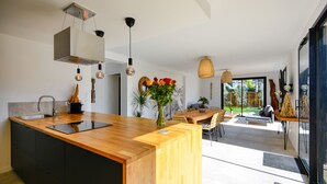 A modern kitchen with a wooden countertop, a built-in sink, and a large island. There is a dining area with a table and chairs, and a large window providing a view of the outdoors. - A 2 pas de la plage, la Villa YIN (Saint-Pierre-Quiberon)