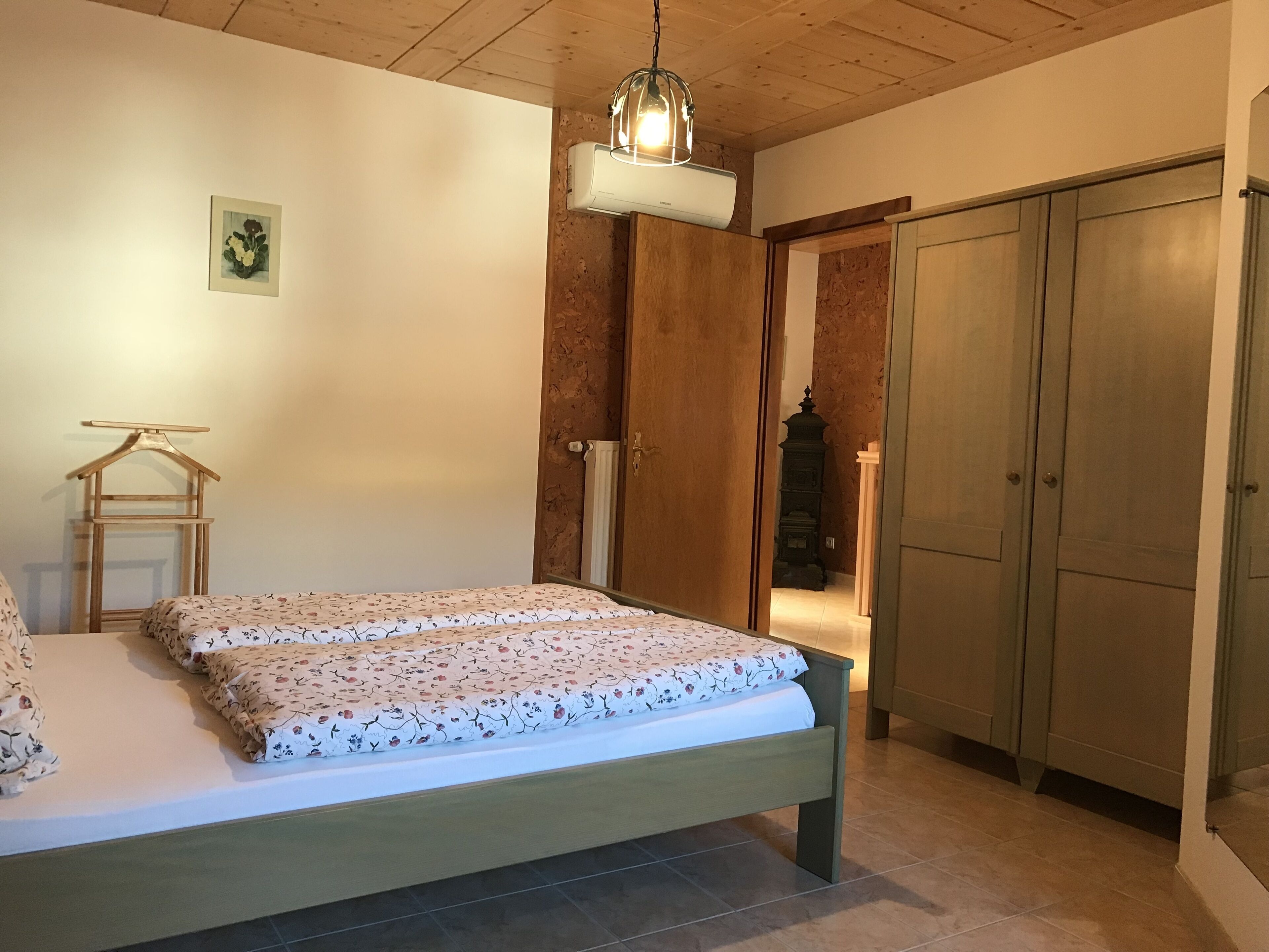 Une chambre à coucher avec un lit, une armoire en bois, un radiateur et un luminaire suspendu.