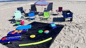 Strandaufbau mit Liegestühlen, Sonnenschirmen und einer schwarzen Matte mit Strandspielzeug.