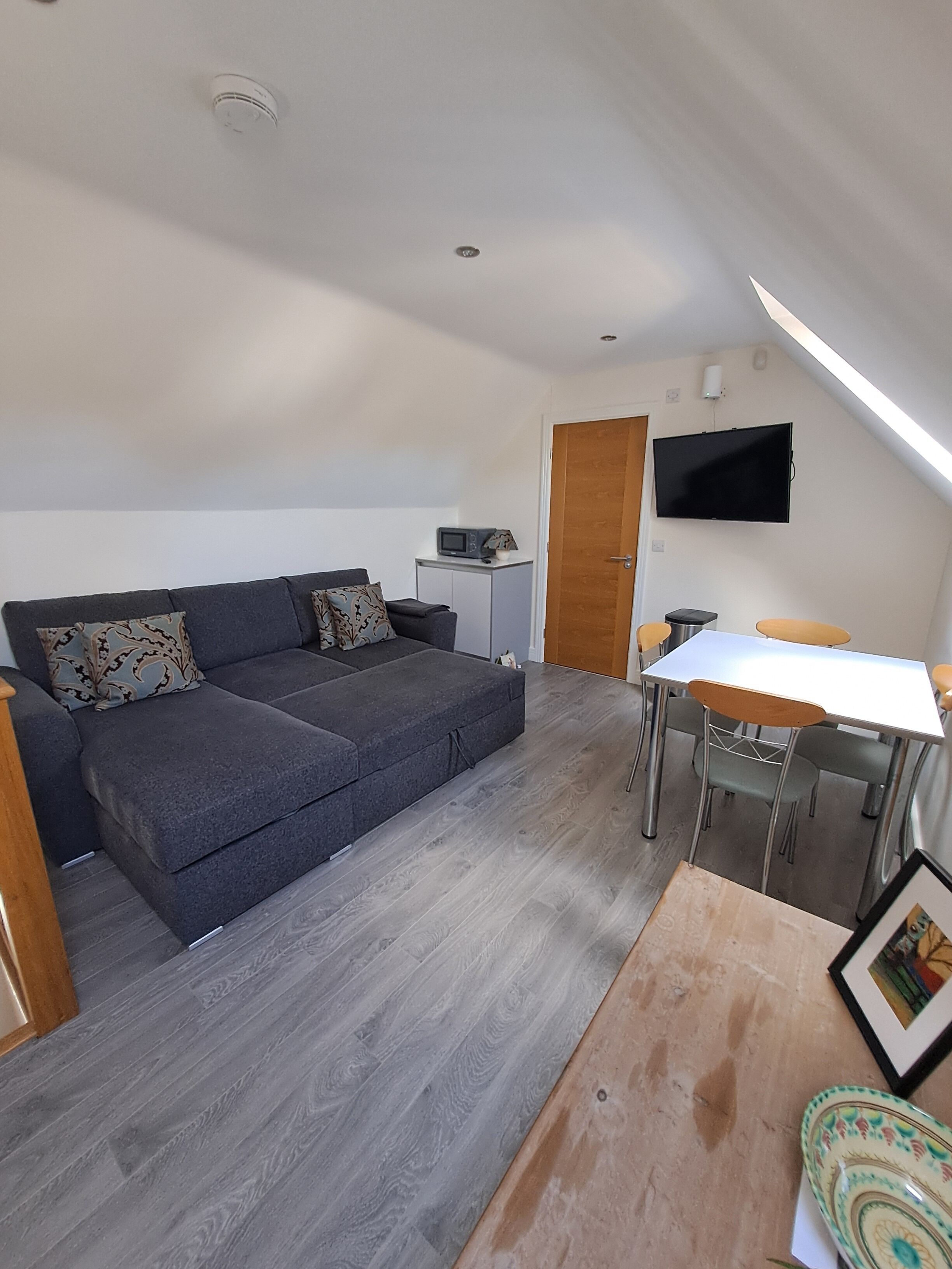 Un espacio habitable compacto con un sofá, una mesita y un televisor instalado en la pared.