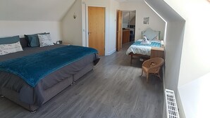 Un dormitori amb un llit gran, una taula petita i una cadira. Hi ha una porta que condueix a una altra habitació.