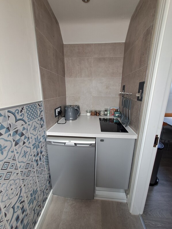 Una kitchenette compacta con lavavajillas integrado, cafetera y una pequeña encimera con diversos utensilios de cocina.