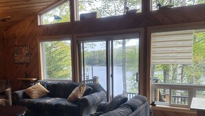 Interno di una baita con un'ampia finestra vista lago, un divano e un tavolo.